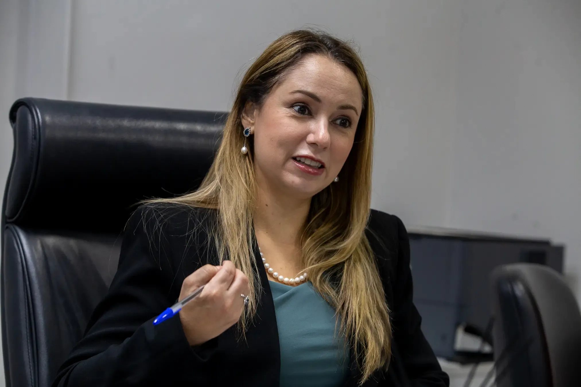 Juiza Ana Graziela é uma mulher branca, com cabelos claros. Ela veste um terno preto com uma blusa azul clara. 